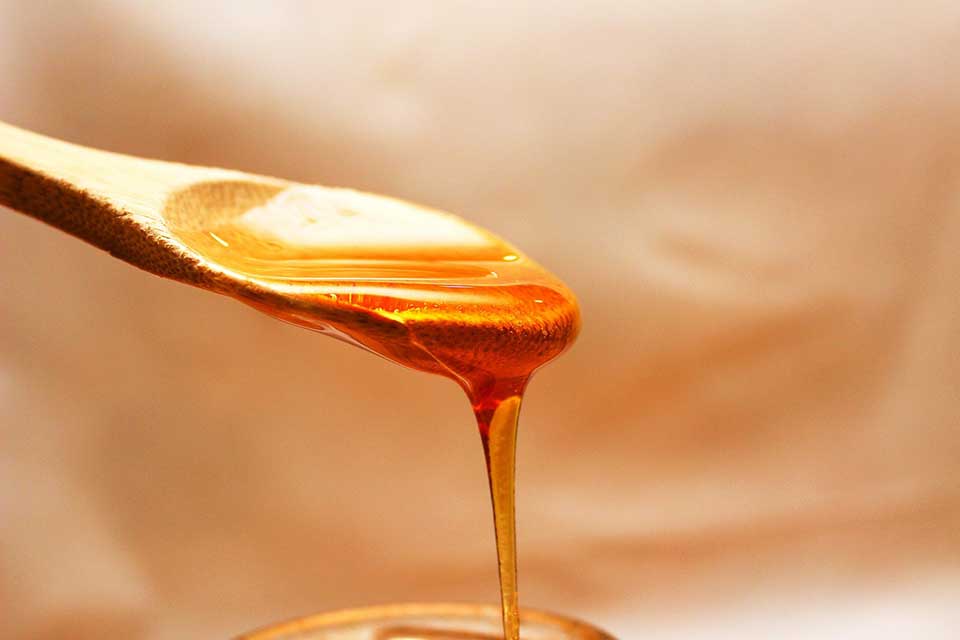Clear supermarket honey dripping from a wooden spoon in the UK