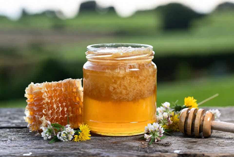 How to tell if honey is real UK – jar of pure raw crystallised honey with honeycomb and wildflowers