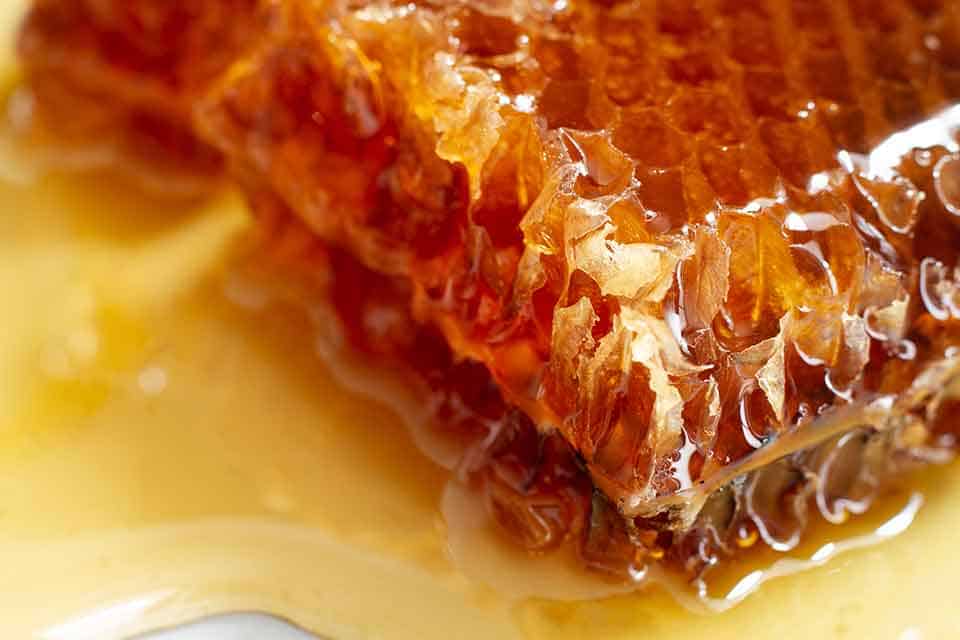 Crude honey dripping from natural honeycomb cells – pure unprocessed honey straight from the hive
